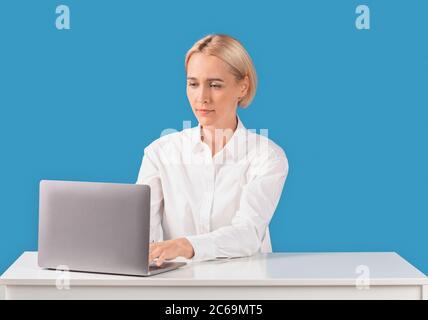 Female office worker using laptop computer at desk on blue background Stock Photo