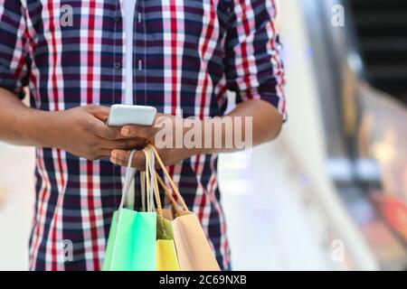 Unrecognizable Black Guy With Shopping Bags In Hands Using Smartphone In Mall Stock Photo
