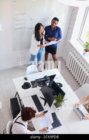 Top view on women in office, discussing new business plan for next month, international team. African woman coach wearing blue office suit look at cam Stock Photo