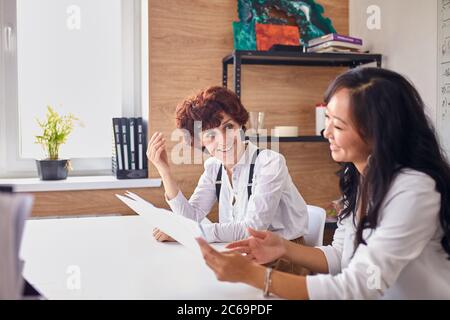 Young and attractive business ladies in office, multiethnic women holding papers about financial information of company. Caucasian woman smiling look Stock Photo