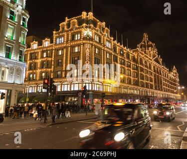 LONDON, UK - 23RD DECEMBER 2015: The outside of Harrods Department Store in London at night during the Christmas Season. People and traffic can be see Stock Photo