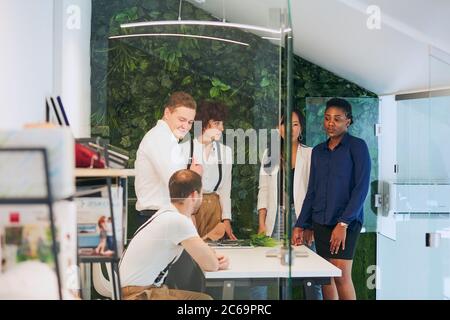 young businesspeople in office boardroom gathered together around white table, discussing their business strategy and sharing information during break Stock Photo
