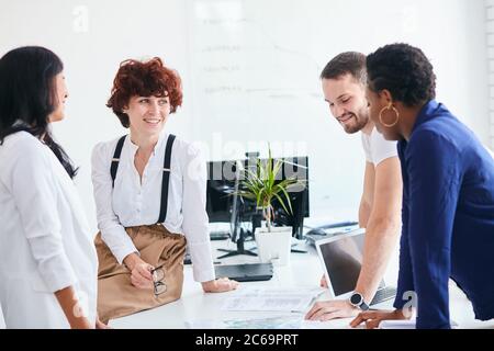 Happy multiracial friends group laugh in office, diverse young colleagues talk enjoying meeting, multicultural people sit at table having fun together Stock Photo
