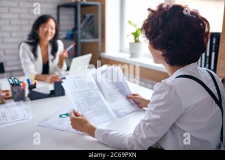 Business for people, cooperation between two sides, asian and caucasian deal. Two business ladies with papers Stock Photo