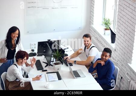 happy creative international team with computers, laptop sitting together looking side Stock Photo