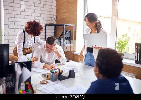 smiling male sit on table while asian woman with laptop speaking. Stock Photo