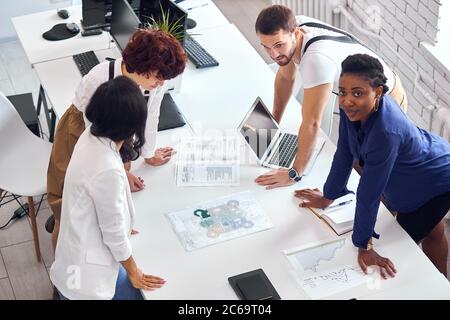 Caucasian, asian, african partners on business project discuss scheme, paper on table. Look at paper on table and think together Stock Photo