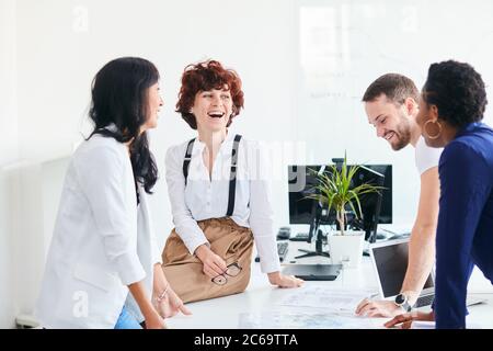 Happy multiracial friends group laugh in office, diverse young colleagues talk enjoying meeting, multicultural people sit at table having fun together Stock Photo