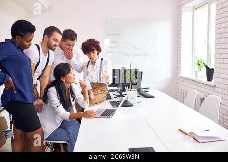 Multiethnic group gathered to look at laptop for discussing project, diverse employees feel euphoric reaching shared goal together Stock Photo
