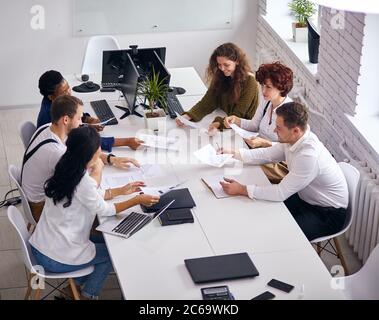 Top view on business partners working on laptop, tablet and documents papers with diagram. Men and women team have brainstorm discussion in white offi Stock Photo