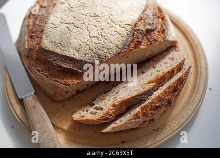 A loaf of rye based sourdough sliced on a bread board with a knife Stock Photo