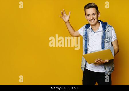Stylish hipster guy in casual outfit posing with a laptop on a yellow background, isolated. Advertising mockup Stock Photo