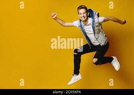 Side view of happy young hipster guy in denim clothes jumping at the yellow background, isolated. Advertising mockup with copy space Stock Photo