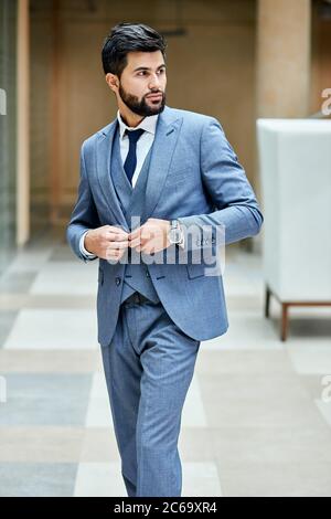 Elegant male in suit posing in street looking away. Attractive brunette in grey suit fastens a button , black haired Stock Photo