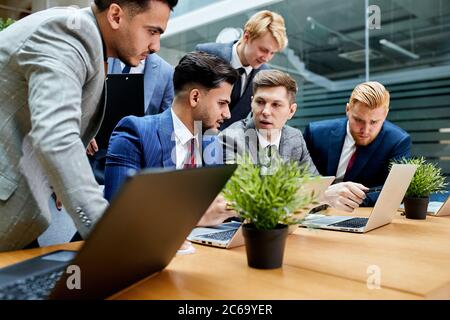 Young men in suits sitting on table with laptop, discuss interesting projects. Potted grass in table Stock Photo
