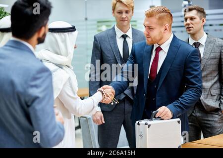 Sheikhs making deal with caucasian man in suit. Two businessmen shaking hands to each other. Business center background Stock Photo