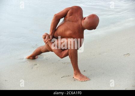 The tanned caucasian man is practicing yoga on the beach Stock Photo