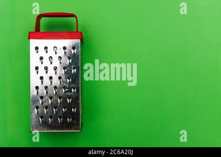 Metal grater with a red handle on a green background. Grater for vegetables and products. Kitchen grater close-up with a copy of the space. A top view Stock Photo