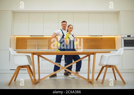 Two co-workers of cleaning company, man and woman stand together after work, after cleaning kitchen. Posing, look at camera Stock Photo