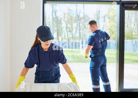 Young janitors invited from cleaning company to clean new house. Two caucasian cleaners in special uniform washing living room Stock Photo