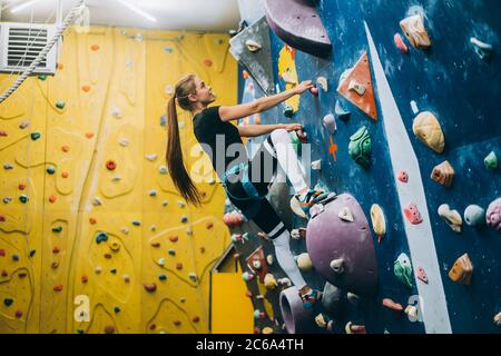 Young woman climbing a tall, indoor, man-made rock climbing wall Stock Photo