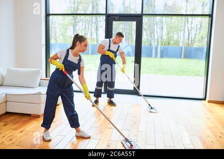Mopping floor in uniform, yellow protective gloves, panoramic window background Stock Photo