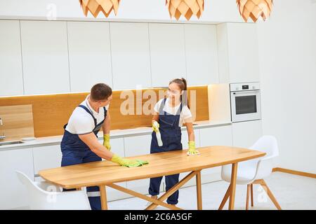 Young caucasian workers of cleaning service working in kitchen together, wiping dust off table. white kitchen Stock Photo