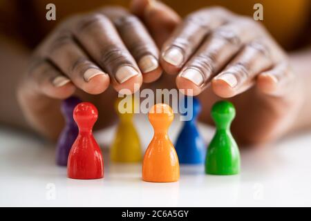 Diversity And Inclusion Concept. Hand Protecting Hand Colored Staff Pawns In Circle Stock Photo