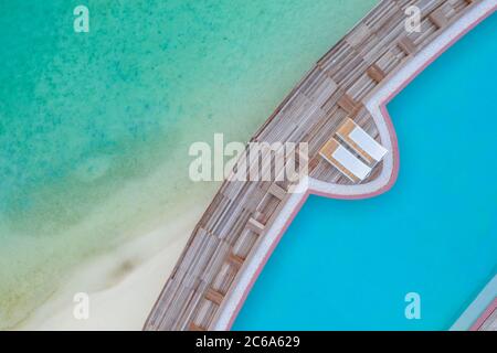 View from drone infinity swimming pool, loungers. Turquoise pool water over sandy beach and ocean lagoon