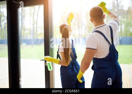 View from back on team of young cleaners make spring cleaning in new house. Two janitors in uniform Stock Photo
