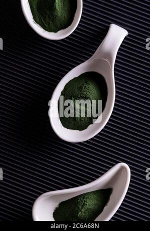 Natural green chlorella or spirulina powder in three differently shaped white porcelain bowls. Healthy superfood eating and dieting concept. Stylish b Stock Photo