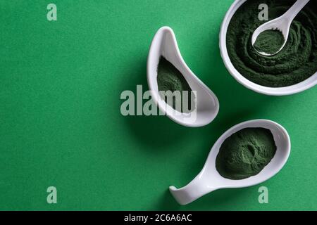 Green chlorella or spirulina powder in three differently shaped white porcelain bowls on green paper background. Healthy superfood eating and dieting Stock Photo
