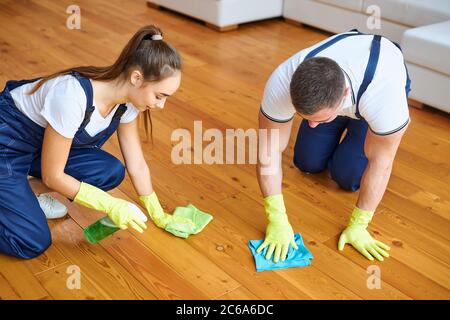 Two cleaners in blue uniforms polishing wooden floor with rag, carefully cleaning wooden floor Stock Photo