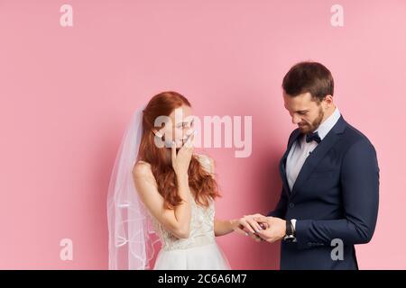 Marriage proposal. Surprised redhaired woman get ring by handsome caucasian man in tuxedo putting ring on her finger. Woman closed mouth with hands. I Stock Photo
