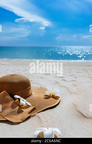 Straw hat with frangipani flowers on white sea sand. With beautiful seascape, the blue sea in the background. background for advertisement of a seasid Stock Photo