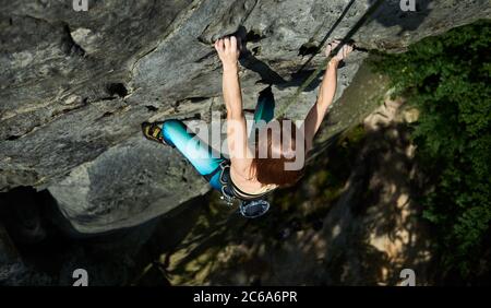 Young woman mountaineer in sportswear climbing alpine ridge. Lady traveler ascending mountain and trying to reach mountaintop. Concept of mountaineering, alpine climbing and extreme sports. Stock Photo