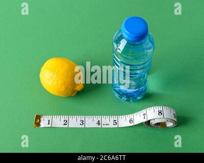 Inch measuring tape, ripe lemon and bottle of pure drinking water on a green background. Concept of healthy eating, diet, weight loss and body slim. Stock Photo