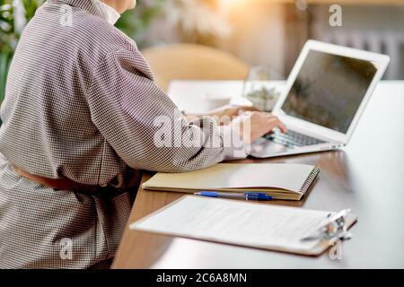 Unrecognizable woman in blazer sit typing on laptop chatting with colleague , papers on table. Isolated in white light room Stock Photo