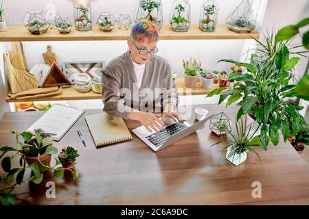 Senior caucasian woman in glasses, with modern colorful hairstyle enjoy working in office, smile at work. using laptop