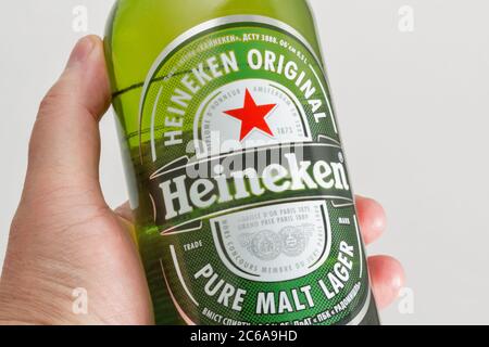 KYIV, UKRAINE - JUNE 17, 2020: Heineken lager beer bottle closeup in human hand against white background. Heineken N.V. is a Dutch brewing company, fo Stock Photo