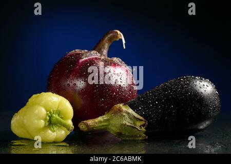 Two eggplants and green bell peppers, with water drops on a dark blue or black background, shot in the Studio. Stock Photo
