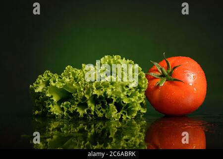 Wet lettuce and tomato with water drops, on a dark green or black background, with a reflection, isolated, shot in the Studio Stock Photo