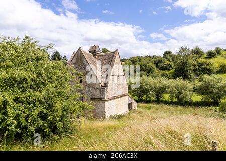 An old stone dovecote (c.1600 AD) beside the infant River Windrush as it flows through the Cotswold village of Naunton, Gloucestershire UK Stock Photo