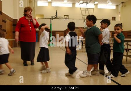 Austin Texas USA, November 2003: Teacher gives the 'shhh' sign to antsy pre-kindergarten students waiting to go through cafeteria line during lunchtime at parochial Catholic school, where the gymnasium does double duty as the lunchroom. ©Bob Daemmrich Stock Photo