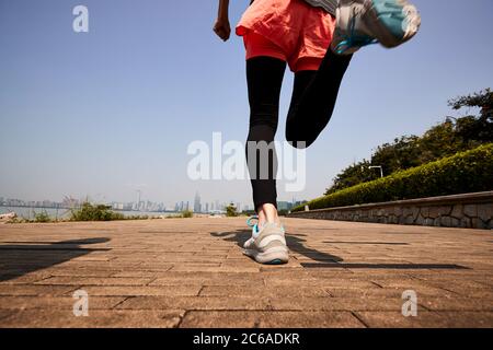 young asian adult woman running jogging outdoors, rear and low angle view Stock Photo