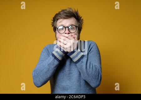Frightened Caucasian man covers his mouth with hands and looks into the camera with big eyes. Stock Photo