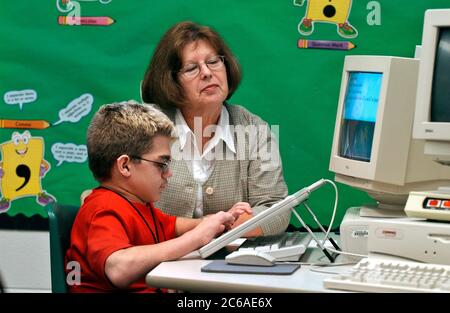 Mabank, Texas September 10, 2003: 12-year-old boy with Hurler's Syndrome with a full-time teacher's aide uses Intellikeys augmentative keyboard to type more easily on a computer in his 7th grade classroom. MODEL RELEASE SP-73 (boy student in red) SP-69 (aide)  ©Bob Daemmrich Stock Photo