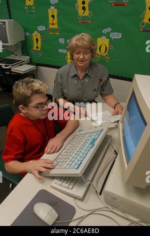 Mabank, Texas September 10, 2003: 12-year-old boy with Hurler's Syndrome with a full-time teacher's aide uses Intellikeys augmentative keyboard to type more easily on a computer in his 7th grade classroom. MODEL RELEASE SP-73 (boy student in red) SP-74 (aide)  ©Bob Daemmrich Stock Photo