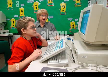 Mabank, Texas September 10, 2003: 12-year-old boy with Hurler's Syndrome with a full-time teacher's aide uses Intellikeys augmentative keyboard to type more easily on a computer in his 7th grade classroom. MODEL RELEASE SP-73 (boy student in red) SP-74 (aide)  ©Bob Daemmrich Stock Photo