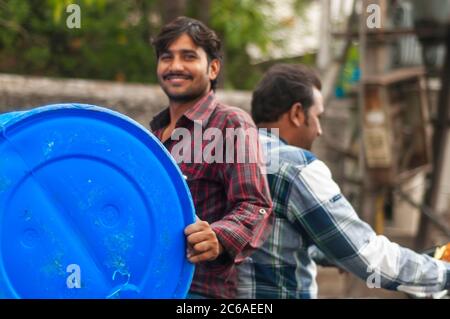 An Indian man riding pillion backwards while carrying a drum. This is an example of 'jugaad' or a non-conventional solution to carry a drum on a bike. Stock Photo